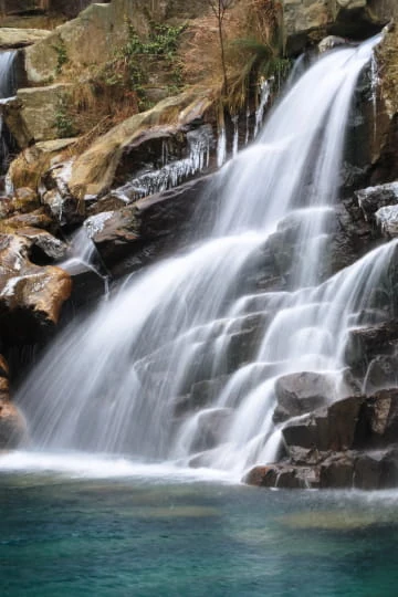 Cascade tropicale se déversant dans un bassin au milieu de rochers et de végétation.